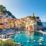 A vibrant, panoramic view of a colorful Italian coastal village nestled into steep cliffs along the turquoise Mediterranean Sea, featuring traditional Mediterranean architecture under a bright, sunny sky.